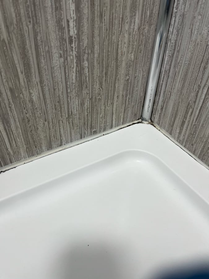 Before: black mould along the silicone where a shower tray meets wood-strip wall panels, Baildon