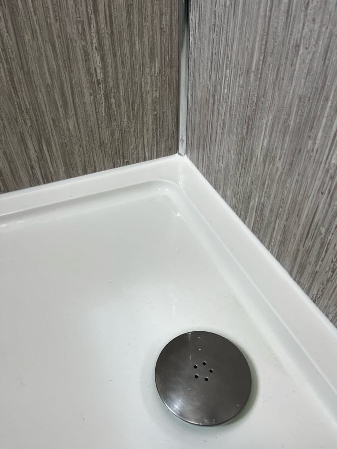 After: clean new silicone bead along a shower tray and wood-strip wall panels, Baildon