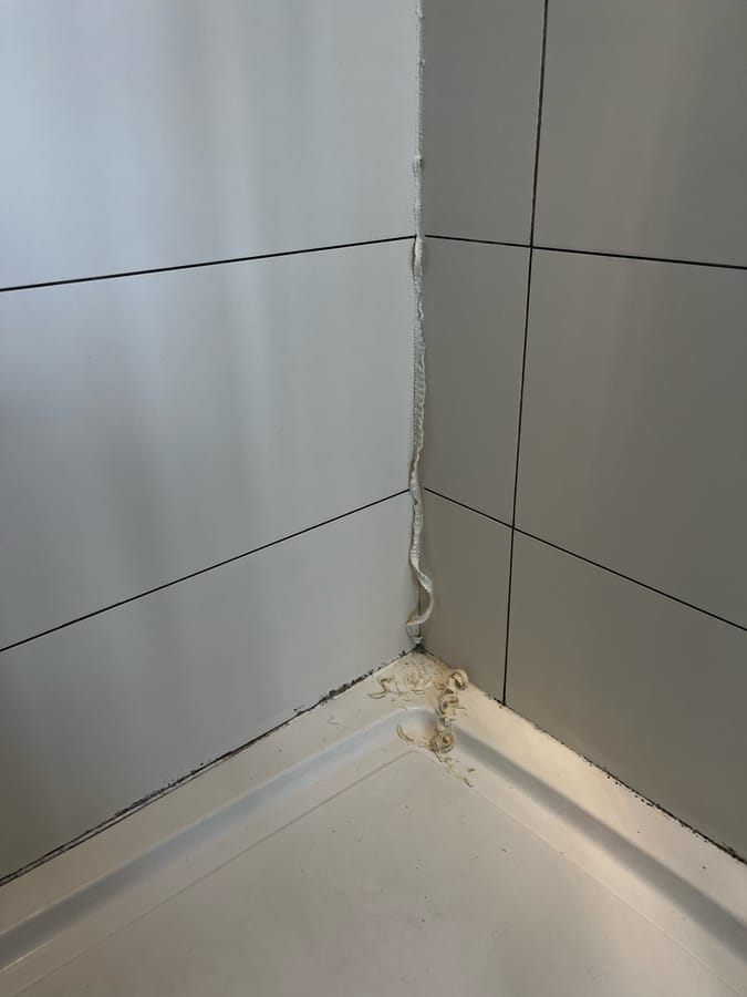 Before: old mouldy silicone being cut out of a shower corner and tray joint, white tiles, Harrogate